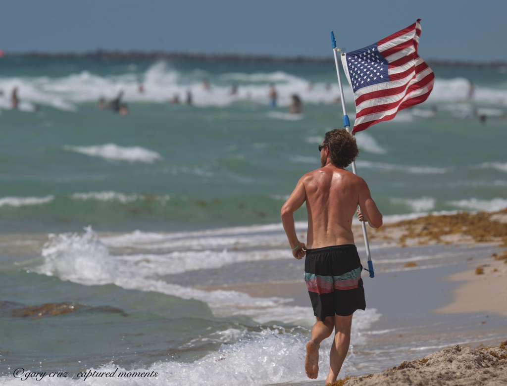 Glen Bradford running with the American flag, photographed from behind, Miami Beach Memorial Day 2026