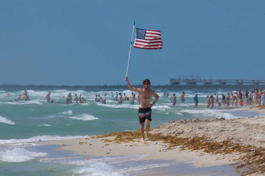 Glen Bradford with the American flag, beach panorama with jetty in the background