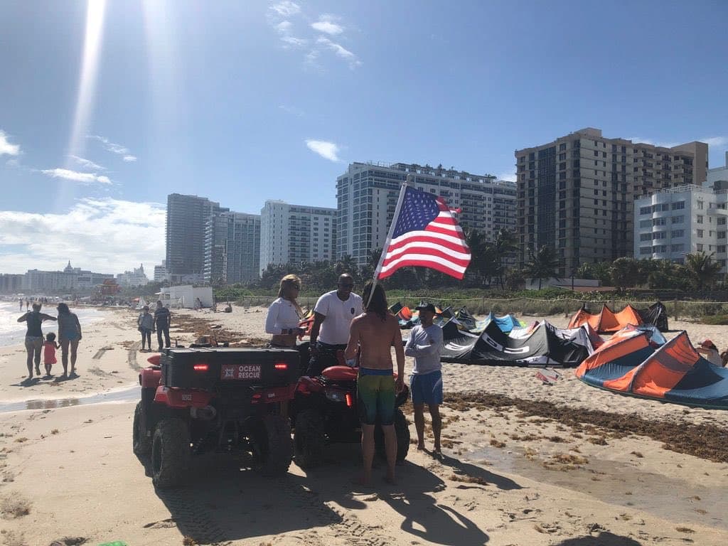 Miami Beach kiteboarding scene with Ocean Rescue ATV, American flag, and kites in the sky