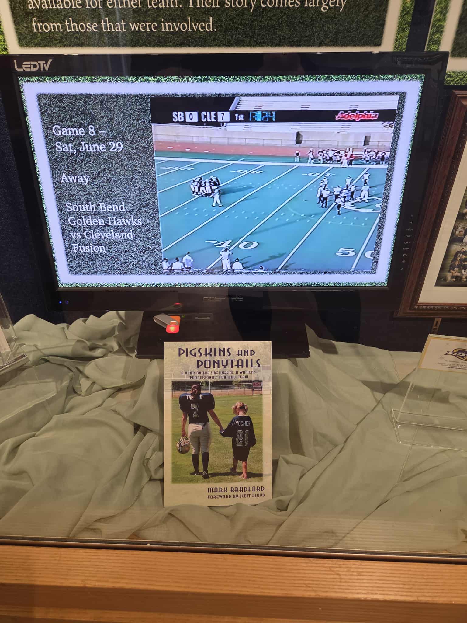Close-up of the Pigskins and Ponytails book and game footage screen in the museum display case